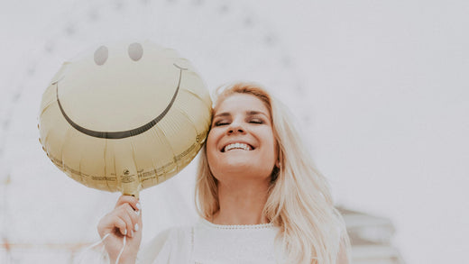 blonde woman smiling and holding a smile face balloon