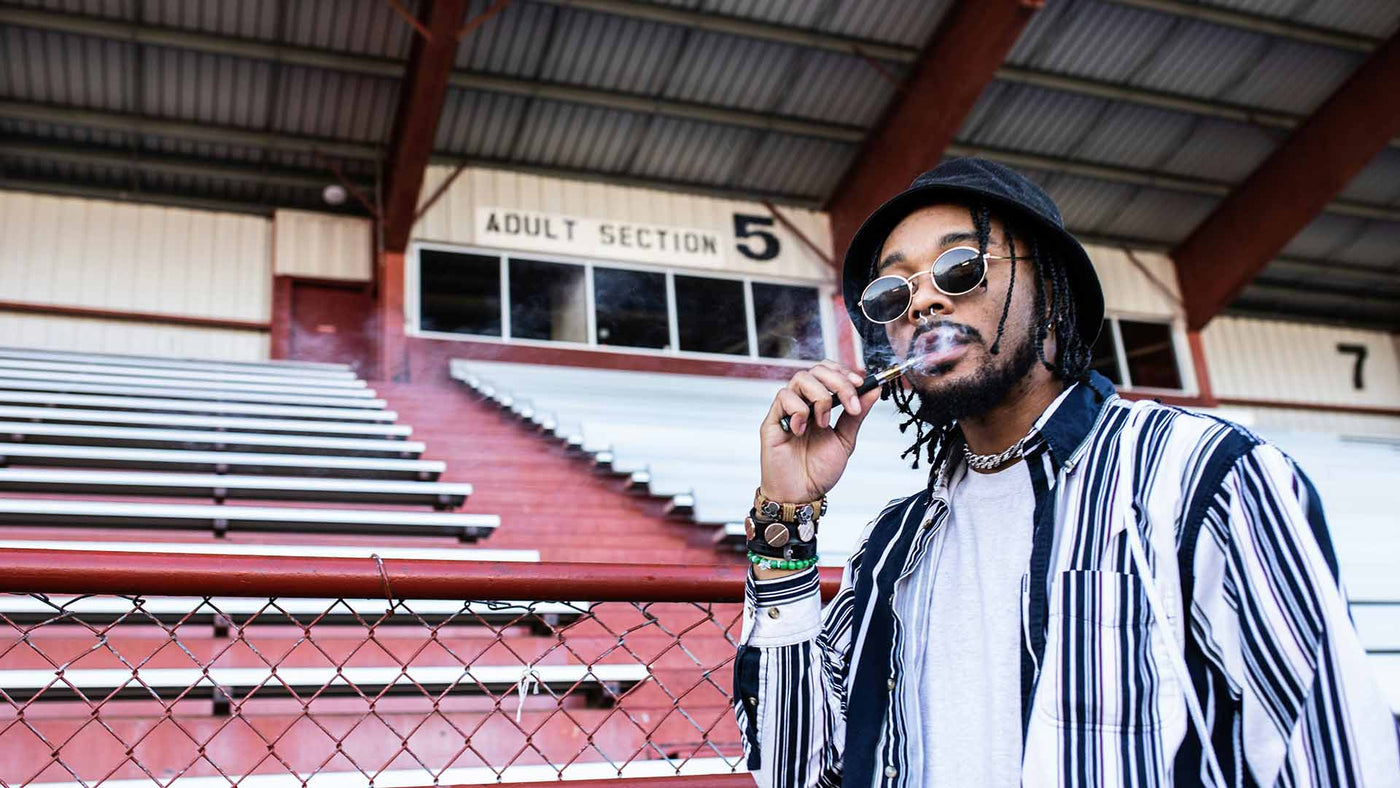 Man vaping in black and white striped zip-up jacket standing near bleachers