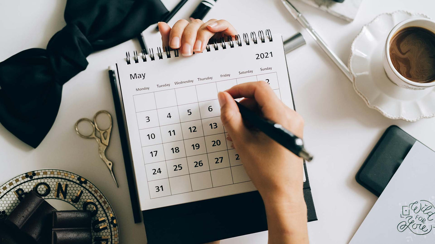 Person writing on a calendar above a cluttered desk