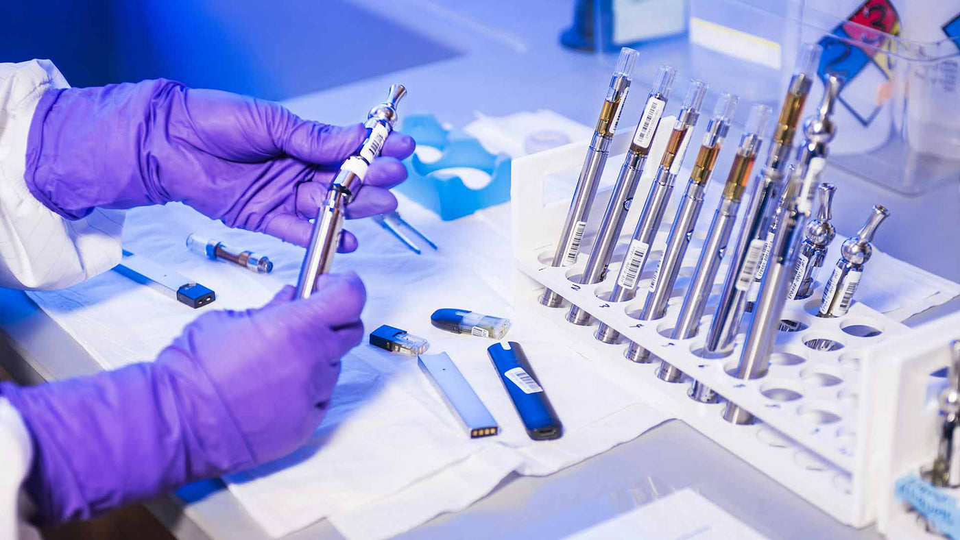 Person in a lab examining a variety of disposable vapes