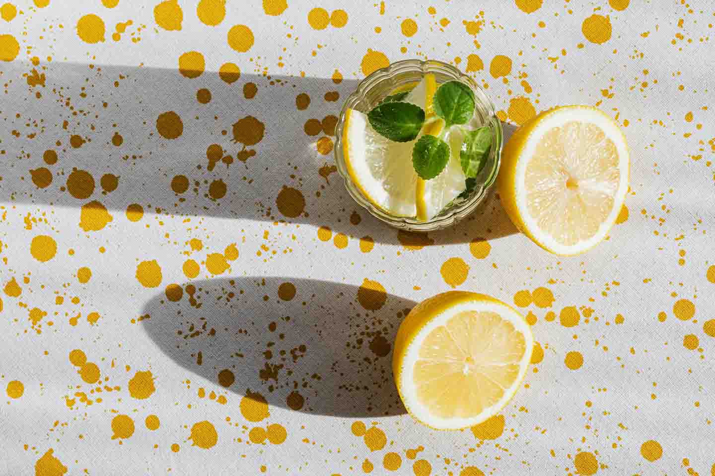 Two cut lemon halves and a glass of lemon water with mint