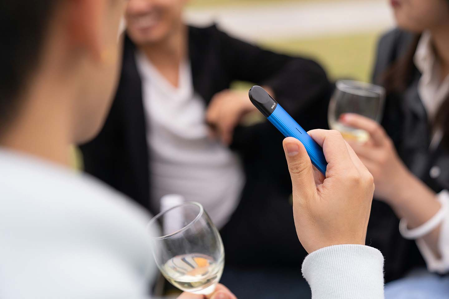 Person holding a blue disposable vape at a social gathering